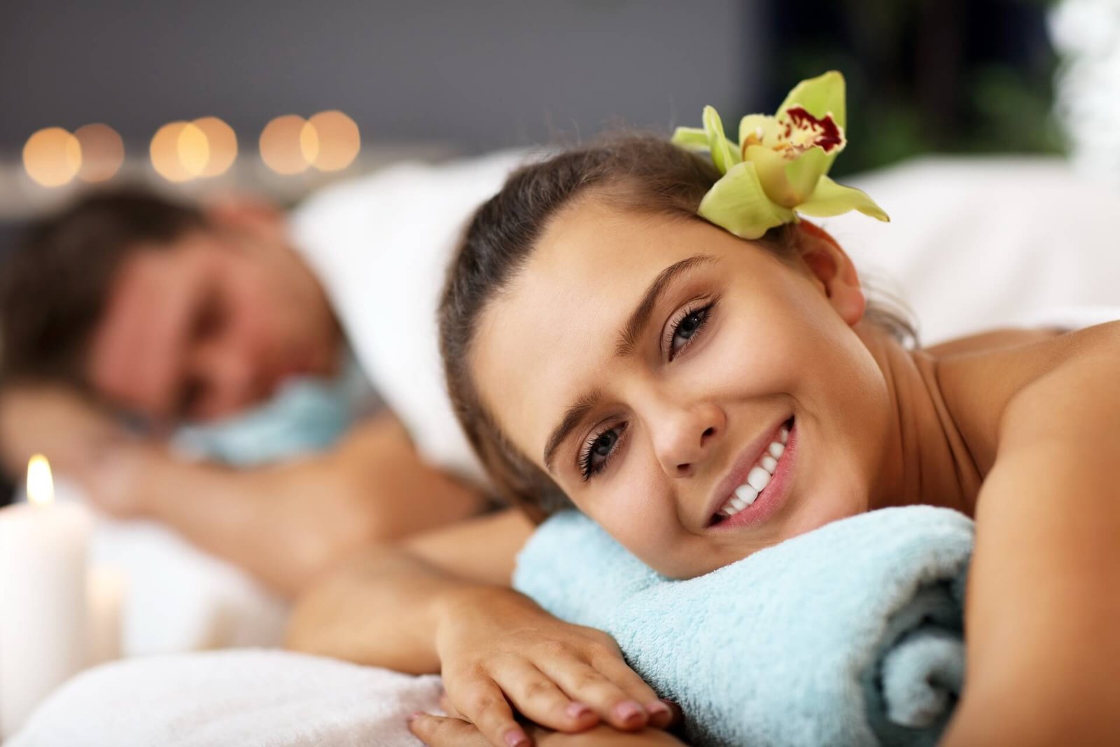 Couples Massage for Your Anniversary A smiling woman relaxes during a couples spa treatment with a flower in her hair.