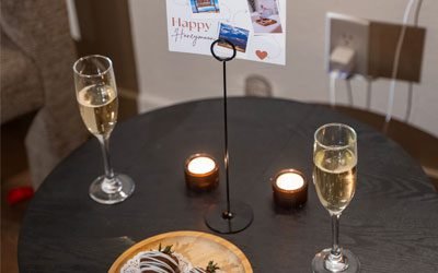 A table set with two glasses of champagne, lit candles, and chocolate-covered strawberries