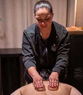 A therapist perfoming a hot stone massage on a man.